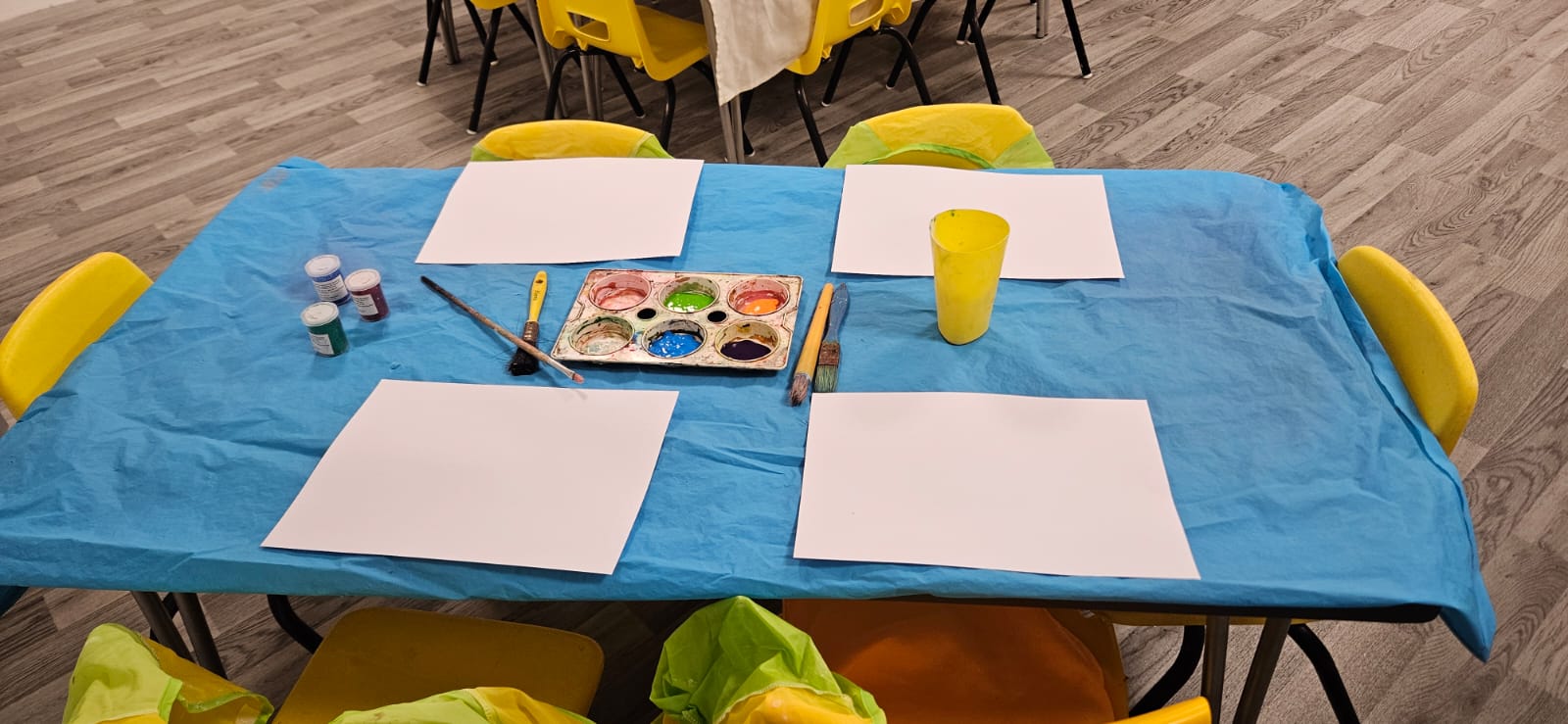 Table set up for painting with paper, brushes and a palette of colours