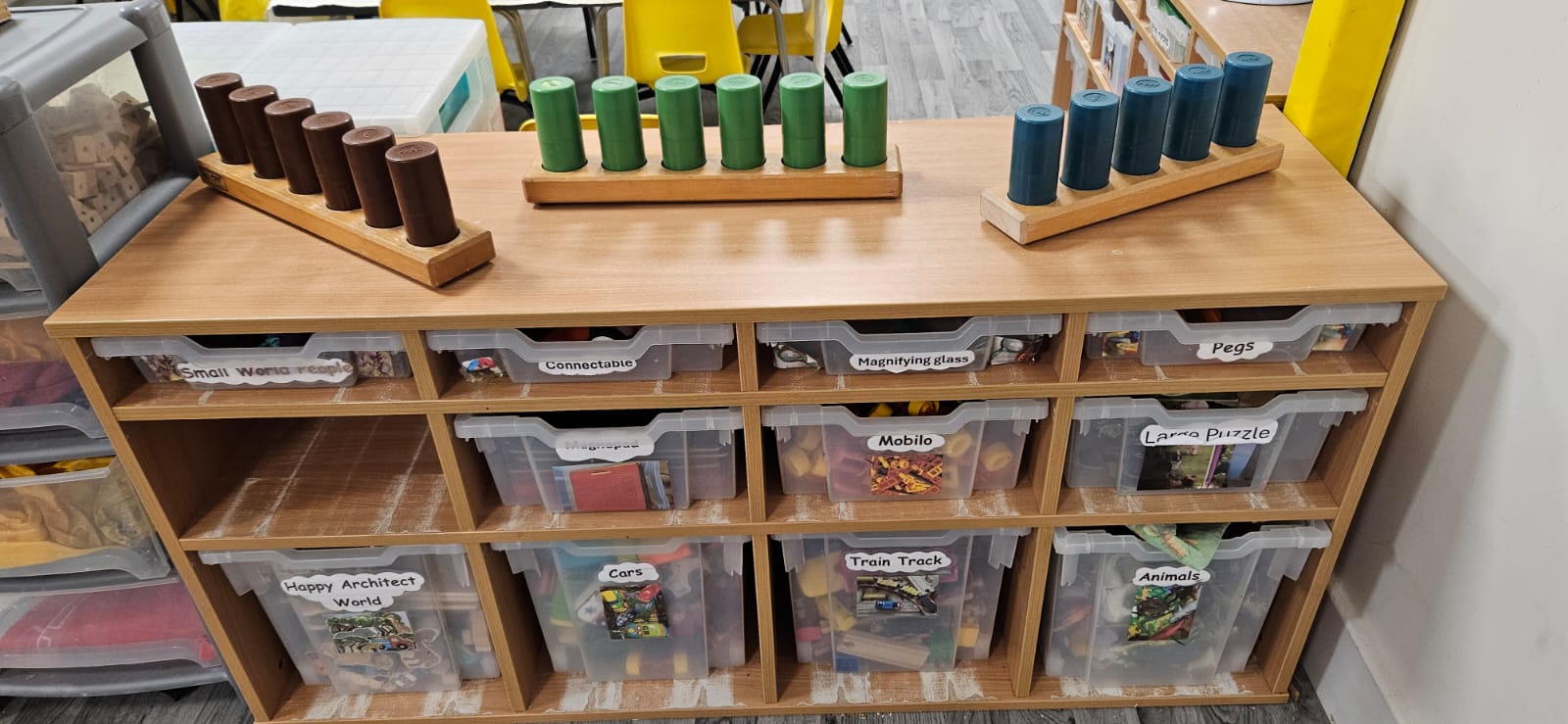 Labelled storage trays of small-world toys with wooden peg resources on top